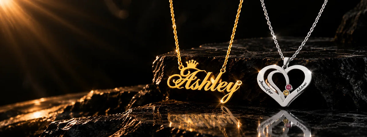 Custom name necklaces — gold "Ashley" script pendant with crown, and silver interlocking heart pendant engraved "Jennifer" and "Adam" with birthstones