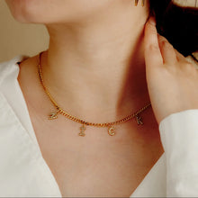 Load image into Gallery viewer, Woman wearing a gold dangling initial necklace with CZ letter charms at the collarbone